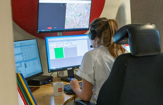 Bildet viser en telefonoperatør som sitter ved det medisinske nødsentralen foran mange dataskjermer.