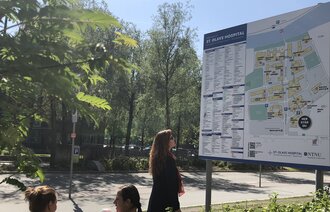 Bildet viser en dame som står foran et digert skilt foran St. Olavs hospital. Skiltet viser informasjon om sykehuset