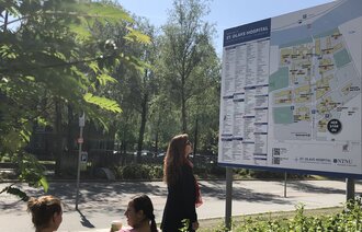 Bildet viser en dame som står foran et digert skilt foran St. Olavs hospital. Skiltet viser informasjon om sykehuset