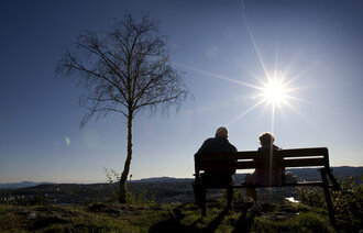 Bildet viser to eldre mennesker som sitter på en benk i motlys
