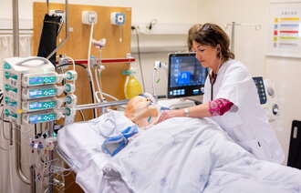 Bildet viser en simuleringsdukke på respirator. En sykepleier står lent over senga.