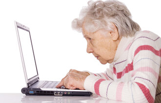 Bildet viser en eldre dame som sitter foran en datamaskin