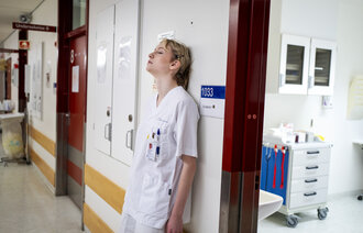 Bildet viser en sliten sykepleier som er lent mot veggen med ryggen.