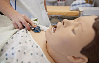 Bildet viser en hånd som holder et stetoskop på brystet til en simuleringsdukke