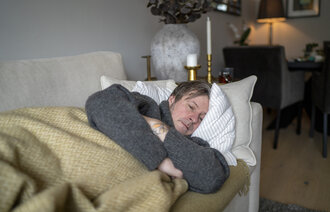 Bildet viser en mann som ligger på sofaen og er syk.