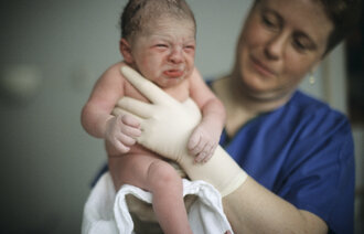 Bildet viser en jordmor som holder opp en nyfødt baby