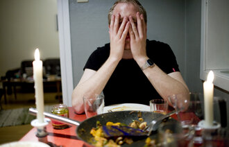 Bildet viser en mann som sitter ved et spisebord og holder seg til ansiktet.