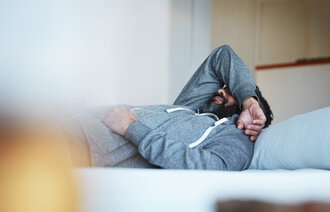 Bildet viser en ung mann som ligger på sofaen med høyre arm over hodet.