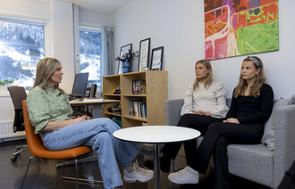 Bildet viser en helsesykepleier på kontoret som sitter i en stolgruppe overfor to ungdommer