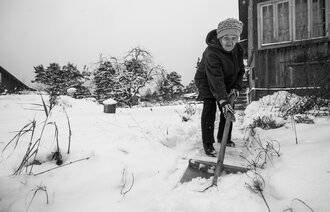 bildet viser eldre dame som måker snø