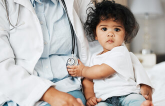 Bildet viser et lite barn som sitter på fanget til et helsepersonell