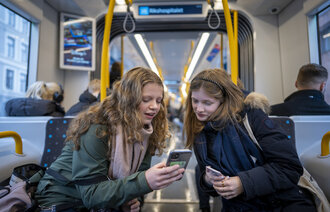 Bildet viser to unge jenter som ser på mobilene sine på trikken.