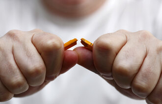 Nærbilde av at en mann knekker en blyant i to.