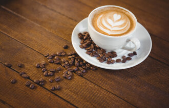 Bildet viser en kopp cappuccino og mange kaffebønner.