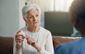 Bildet viser en kvinnelig pasient som tar medisiner med en sykepleier til stede