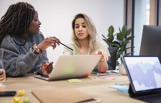 Bildet viser to kvinner som sitter og diskuterer foran en PC