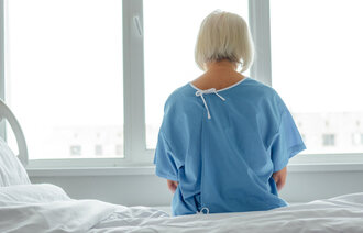 Bildet viser en pasient bakfra. Hun sitter på en sykehusseng og ser framfor seg.