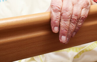 Bildet viser en hånden til en eldre mann som ligger i sengen på et pleiehjem.