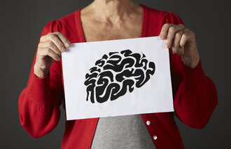 Bildet viser en eldre kvinne som holder opp en tegning av en hjerne.
