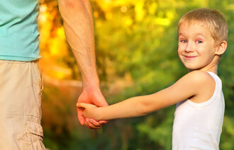 Bildet viser en smilende gutt som holder sin far i hånden