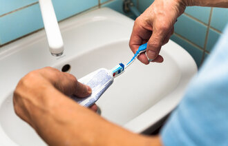 Bildet viser to hender som tar tannkrem på en tannbørste.