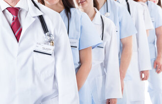 Bildet viser en rekke med leger og sykepleiere som står på rekke bak hverandre. Kun overkroppen synes.