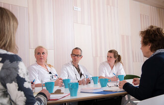 Bildet viser helsepersonell som sitter rundt et bord. Noen har uniform, andre ikke.