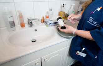 Bildet viser en hjemmesykepleier med en urinstrimmeltest på badet til brukeren
