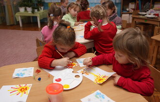 Barn i en barnehage som sitter rundt små border og tegner.