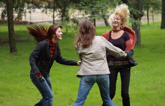 Tre kvinner danser i ring ute i en park