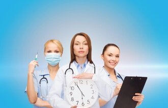 Bildet viser tre sykepleiere. Den i midten holder en klokke.