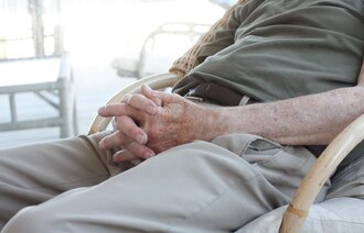 Bildet viser deler av en eldre person som sitter med hendene i fanget.