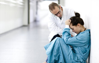Bildet viser en kvinnelig sykehusansatt som får trøst av en mannlig i en korridor.