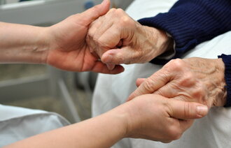 Bildet viser hendene til en sykepleier som holder hendene til en eldre person.