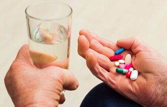 Bildet viser to hender, den ene holder i et glass vann, den andre en håndfull tabletter.