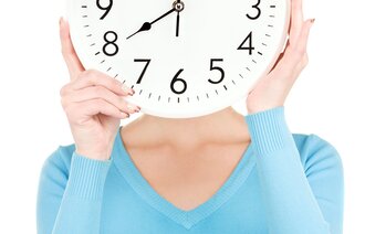Bildet viser overkroppen til en kvinne som holder en klokke foran ansiktet.