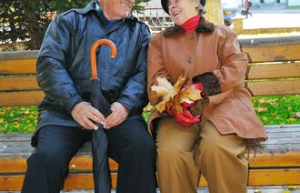 Bildet viser to eldre mennesker som sitter på en benk og ler.
