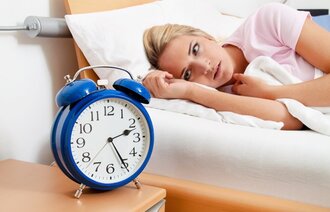 Bildet viser en kvinne som ligger i sengen og ser på vekkerklokken.