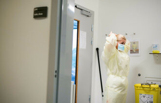 Bildet viser en sykepleier som står i en sluse inn til et isolat og tar på seg gul smittefrakk.