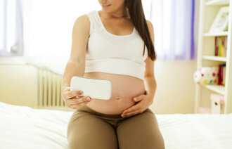 Bildet viser en gravid kvinne som sitter på sengekanten mens hun tar bilde av sin gravide mage.