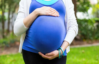 Bildet viser en gravid kvinne med blå topp som holder rundt magen sin