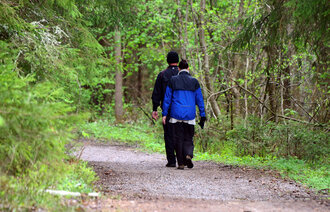 Bildet viser to personer sett bakfra som går tur i skogen.
