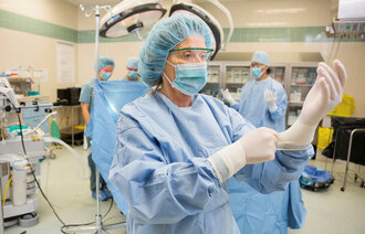 Bildet viser en kvinnelig operasjonssykepleier som tar på seg hansker før en operasjon