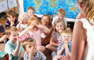 Bildet viser barn i en barnehage som ler sammen med en førskolelærer.