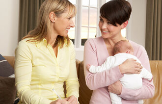Bildet viser et hjemmebesøk, en helsesøster som besøker en mor og hennes nyfødte barn hjemme.
