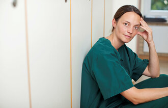 Bildet viser en sykepleier som sitter i en gang og ser tankefull ut
