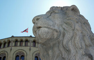 Bildet viser Stortinget og den ene løvestatuen utenfor.