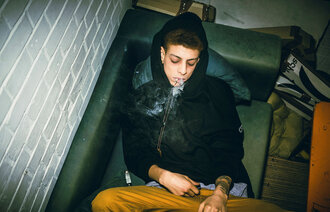 Bildet viser en ung mann som ligger på en sofa og røyker en joint