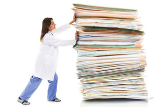 Bildet viser en kvinnelig helsearbeider som dytter på en kjempestor stabel med dokumenter og mapper