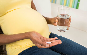 Bildet viser en gravid kvinne som holder frem en tablett og et glass vann